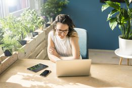 Smiling freelancer sitting at desk in loft looking at laptop