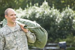 Caucasian soldier carrying duffel bag outdoors.