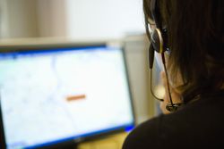 Emergency services dispatcher wearing a headset in front of a computer.