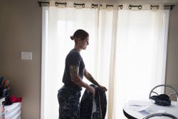 Military woman putting on fatigues in her house