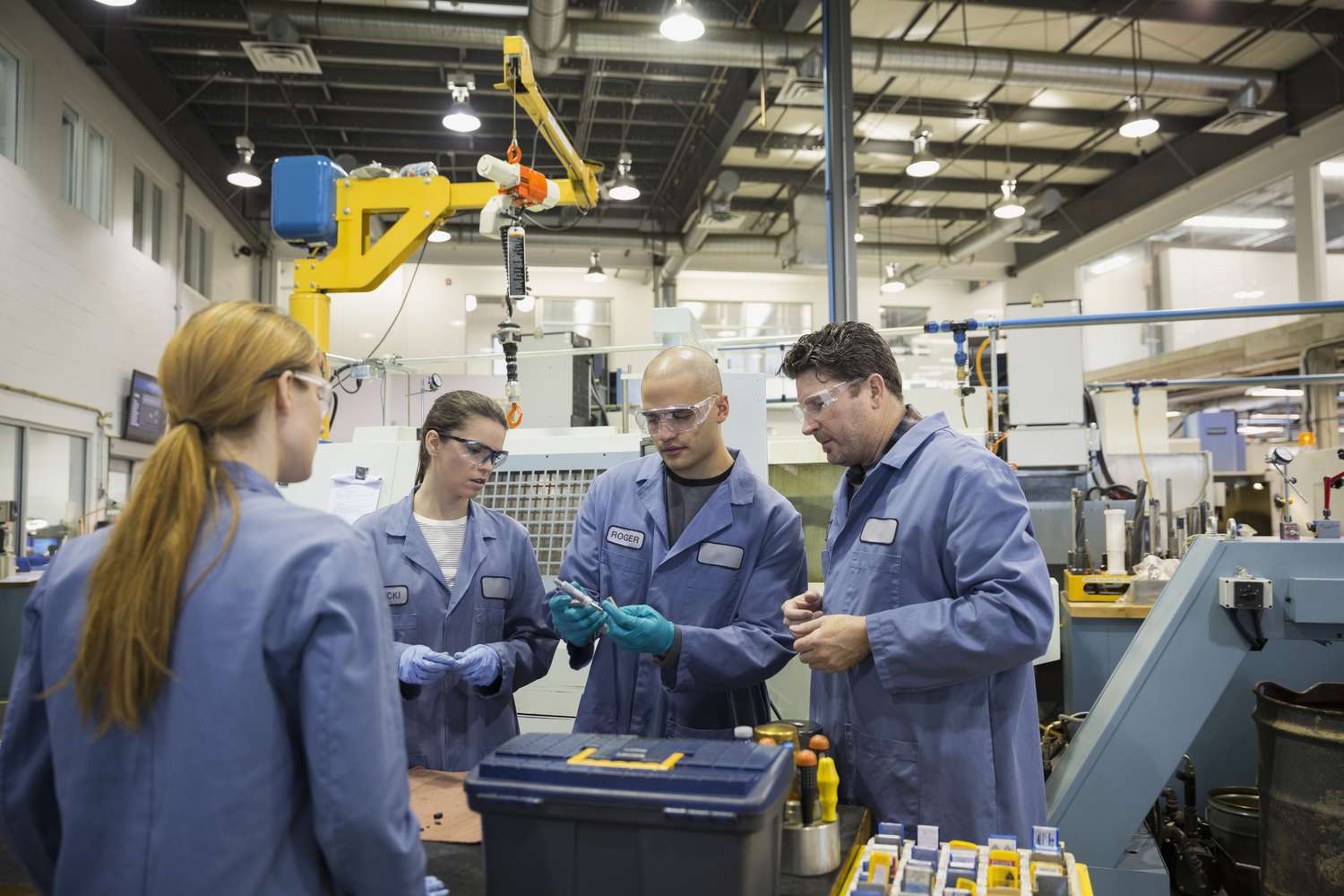 These four factory workers wear jackets over their street attire in an industrial setting.