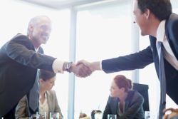 two businessmen shaking hands, two businesswomen sitting in the background