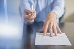 Person sitting at office desk presenting ballpen and contract