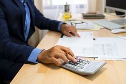 Tax examiner working at office desk using a calculator to verify numbers