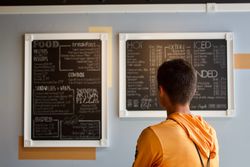 Man reading a restaurant menu written on chalkboards in a cafe.