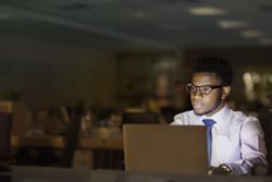 An attorney reading legal websites on a laptop at night in an office