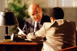 Mature executive sitting at desk, talking to young man