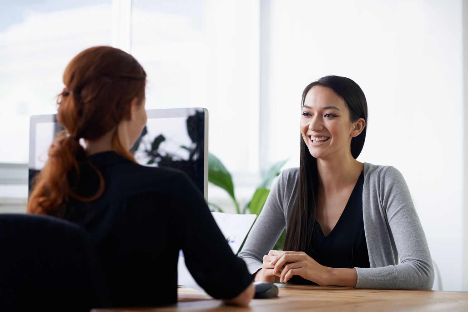 Two employees sitting across a table from each other speaking and building emotional intelligence which leads to efficiency.