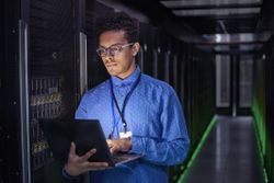 technical support engineer standing in server room with laptop