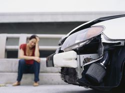 Woman sitting on curb with head on her hand after an accident and before filing an insurance claim.