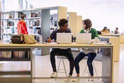 Colleagues discussing while studying through laptop computers in library