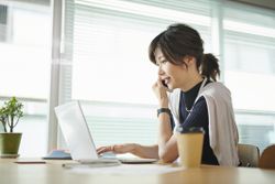 A woman is talking on her cell phone while working on a laptop.