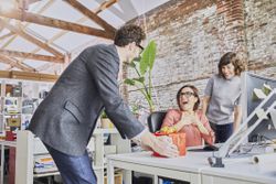 Man giving a gift to a woman sitting at her desk.