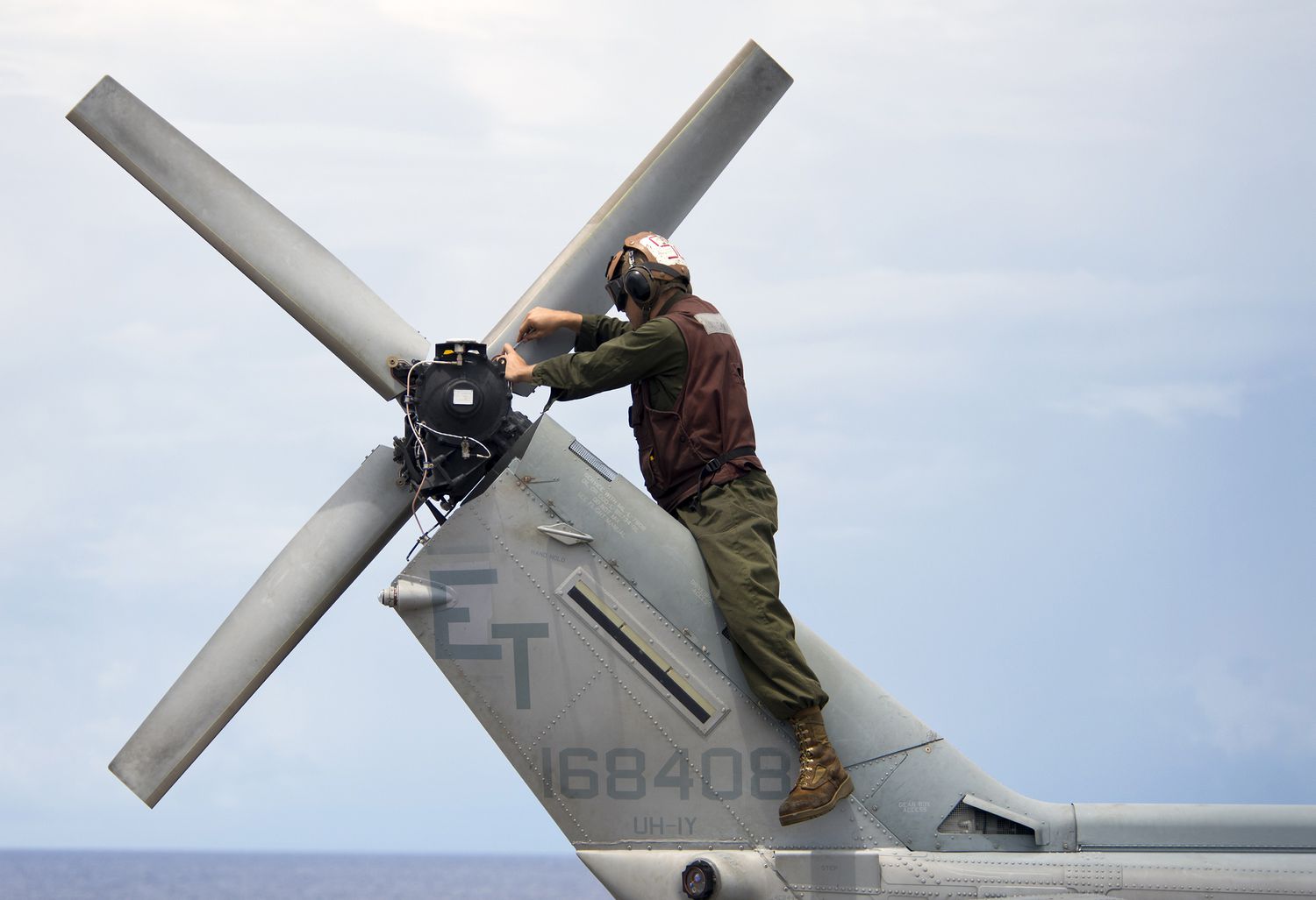 A Marine conducts maintenance on the tail of an UH-1N Huey helicopter.