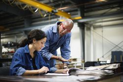 Female manager and male worker talking at desk in factory