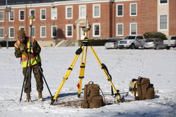 Geographic Intelligence Specialist setting up equipment outside a building on a snow covered field.