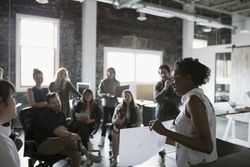 Female architect with blueprint leading meeting in open plan loft office