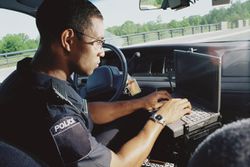 Police information technology officer entering crime scene information into car-mounted laptop