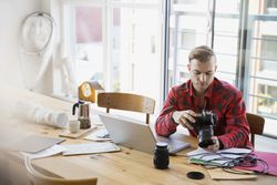 Photographer with camera uploading to laptop at table