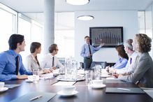 Businessman giving PowerPoint presentation to table of executives