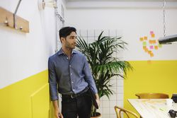 Young man waiting for an interview leaning against a wall and holding a portfolio.